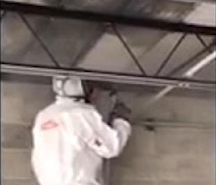 SERVPRO employee in PPE, soda blasting a soot covered ceiling